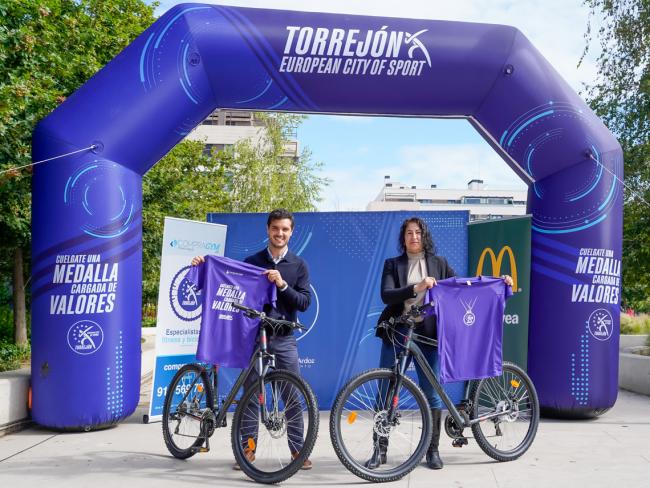 El alcalde, Alejandro Navarro Prieto, y la concejala de Deportes y Turismo, Mirian Gutiérrez, presentando la iniciativa en el Recinto Ferial, con dos bicicletas y el regalo que se va a dar a los participantes: una camiseta conmemorativa de Torrejon, Ciudad Europea del Deporte 2026